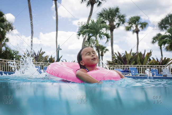 A little girl in an inflatable tube splashes in a pool