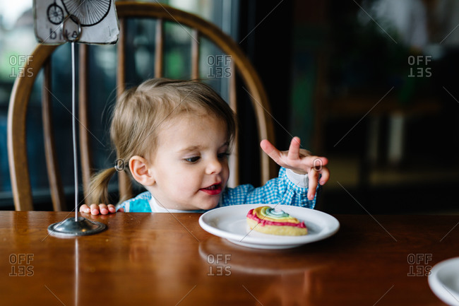 A little girl eats a rainbow cookie at a restaurant
