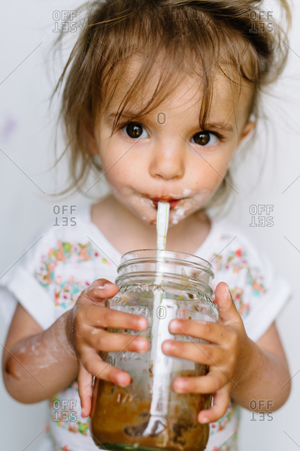 A little girl drinks a chocolate milkshake from a jar