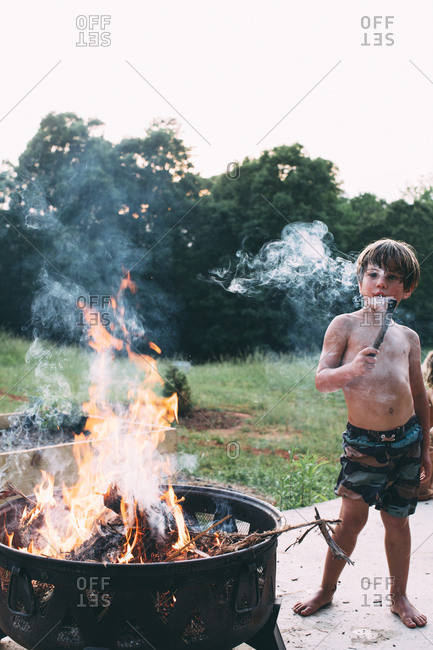 A boy holds a smoking stick next to a fire pit