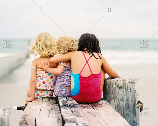 Three young girls sitting with arms around each other on dock