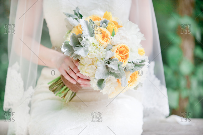 A yellow, white and silver bouquet of flowers in bride\'s hands