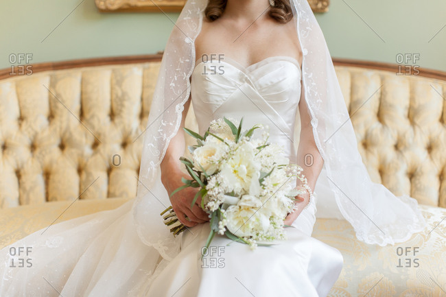 Bride wearing a lace veil and white gown seated on an elegant sofa