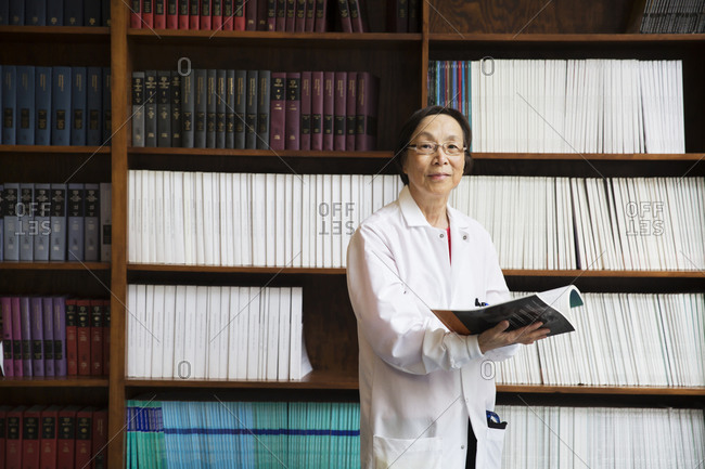 Scientist with book by bookshelf
