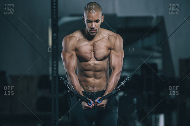Young man training pectoral muscles at cable crossover in gym