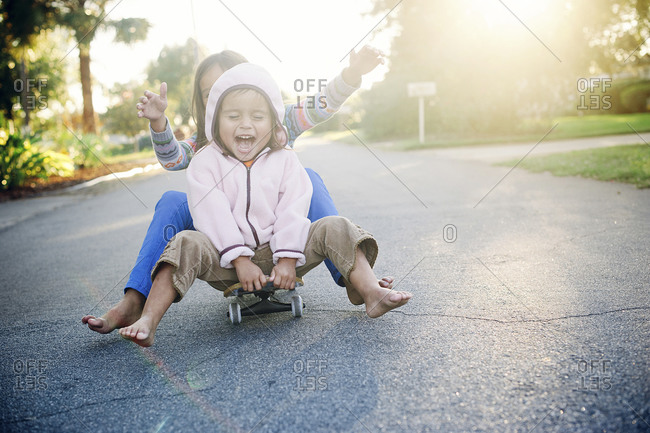 Two young girls riding down a street seated on skateboard