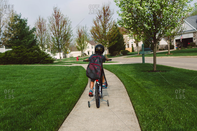 Boy on bike with training wheels in suburb