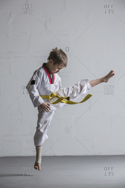 Karate boy kicking in air against white wall