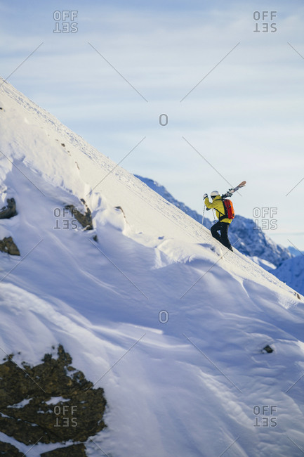 Man carrying skis on a steep mountain slope in Austria