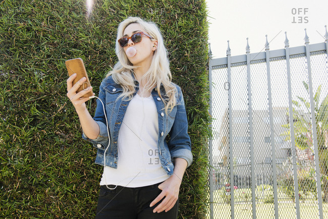 Blonde woman using her smartphone while blowing a bubble