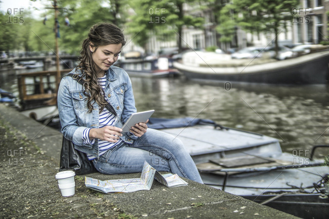 Female tourist using digital tablet in front of town canal, Amsterdam