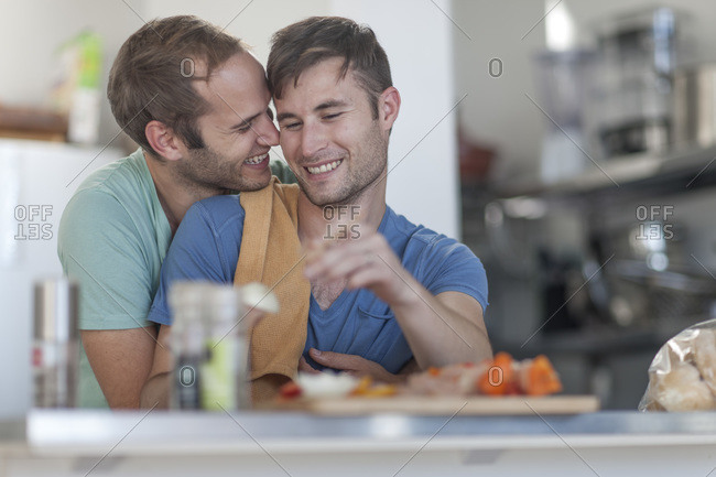 Happy gay couple preparing meat skewers in kitchen