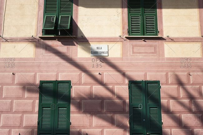 Facade of a pink building  with green shuttered windows in Italy