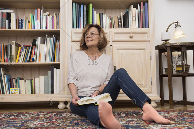 Senior woman sitting on the floor in front of bookshelf and reading