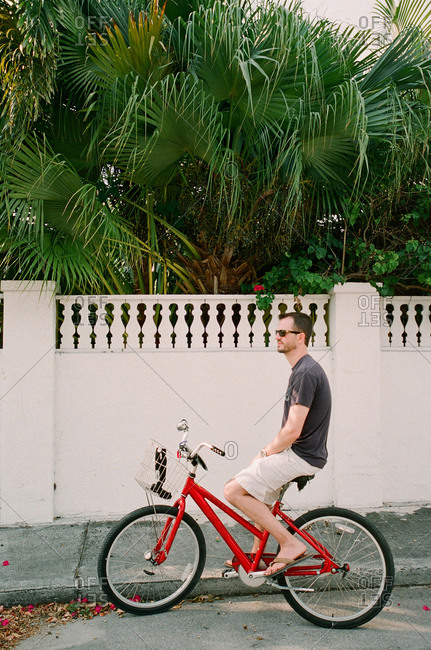 Man sitting on a red bicycle before a wall with tropical vegetation