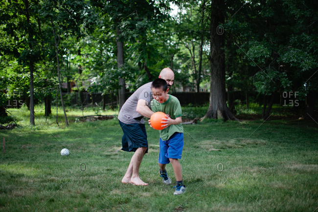 Dad and boy wrestling over ball in yard
