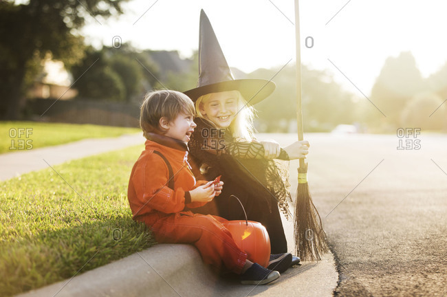 Siblings sitting on a roadside in Halloween costumes