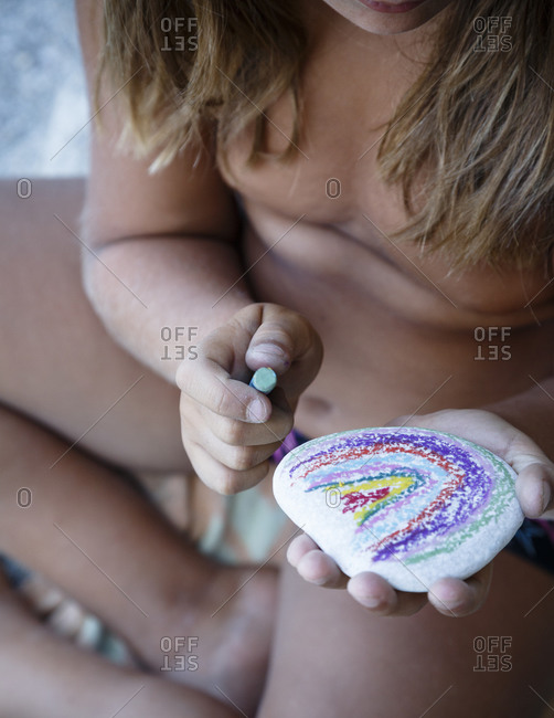 Kid painting on a sea pebble at Parisena beach in Horefto, Pelion peninsula, Greece