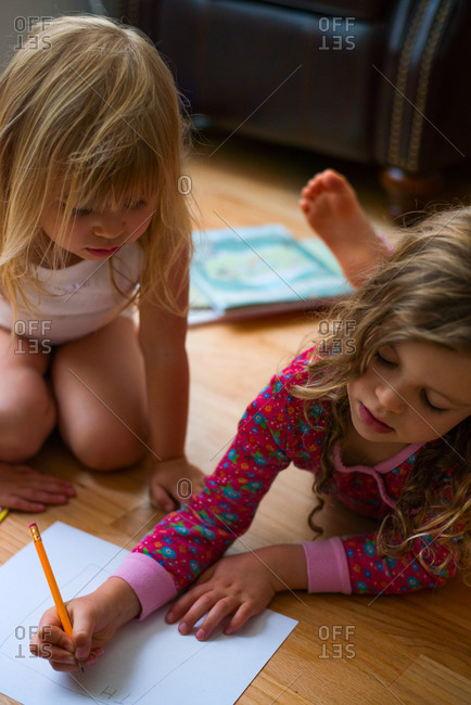 Young girl watches her sister write with a pencil on paper
