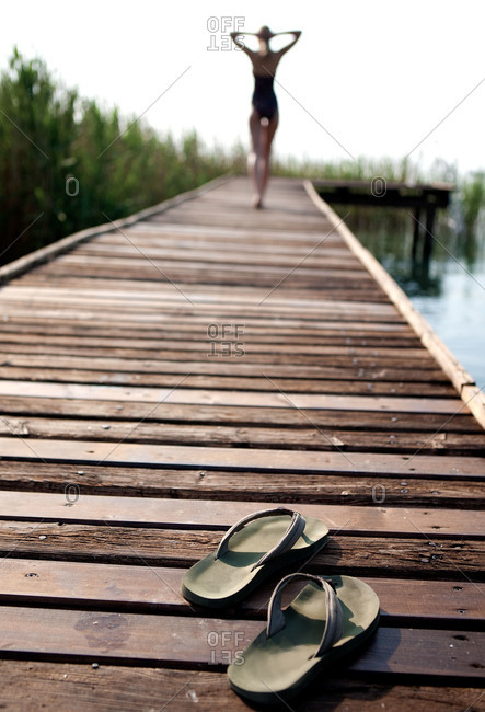 A woman walks down a pier leaving her flip flops behind