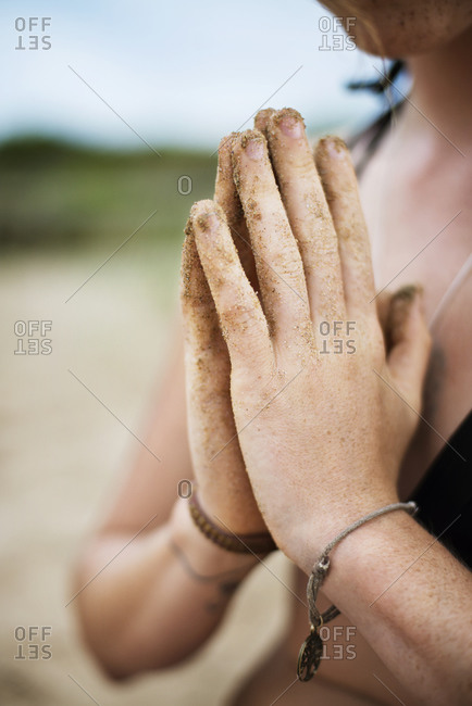 A woman with sandy hands engages in a prayer pose