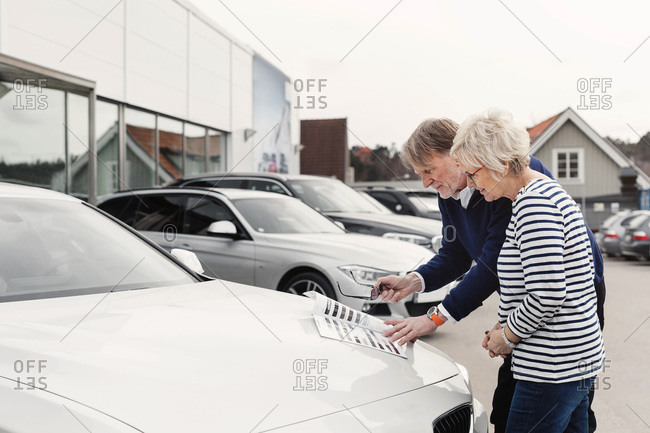 Senior couple reviewing brochure on car outside showroom