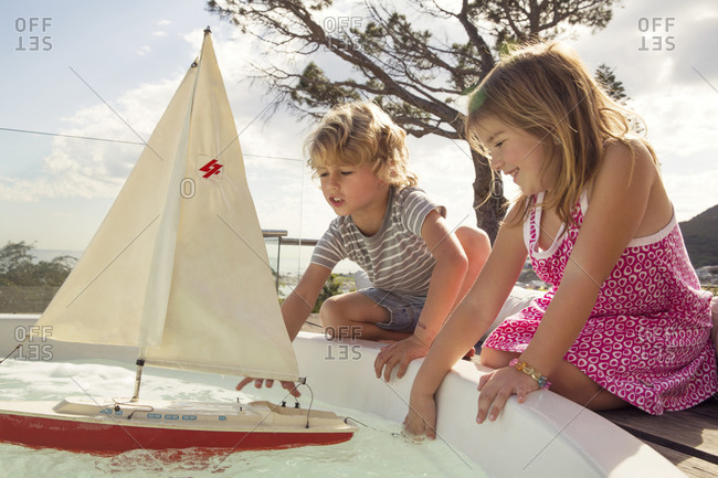 Girl and boy crouching to play with a toy sailboat