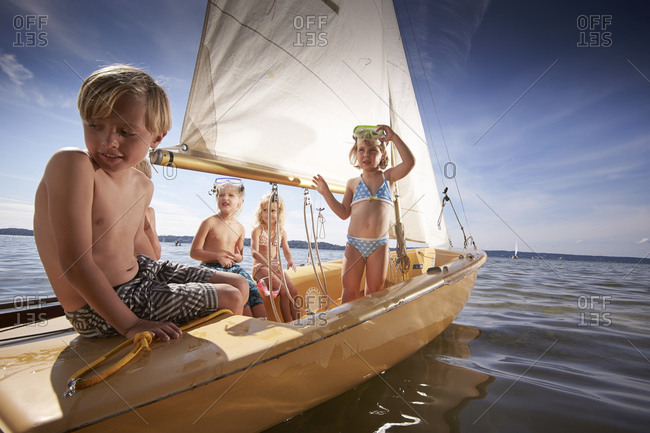 Four children sailing a small sailboat on lake