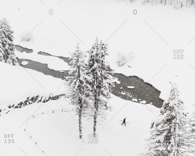 Aerial view of man walking past a stream in a snowy landscape