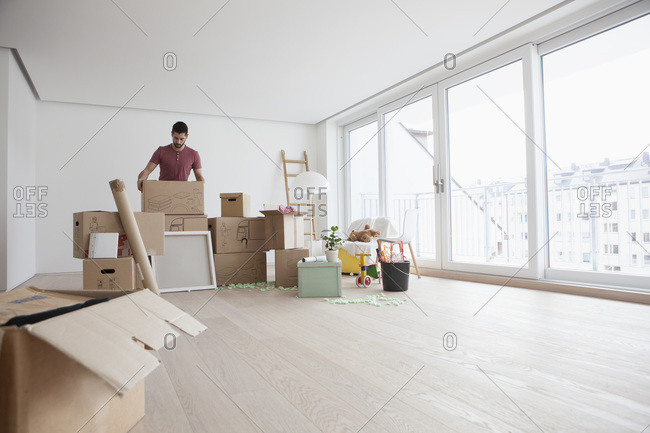 Young man in new flat unpacking cardboard boxes