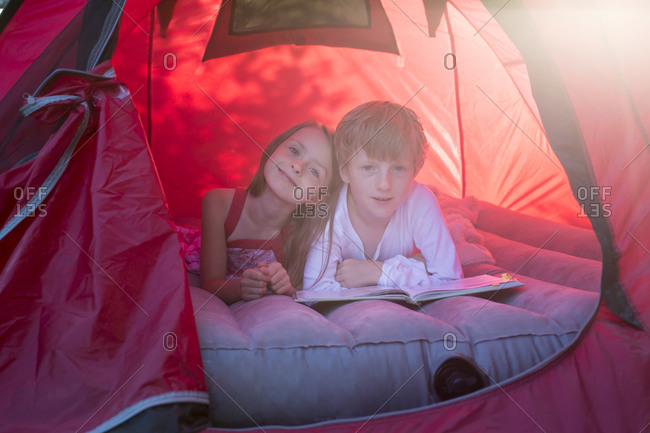 Portrait of brother and sister lying in a red tent with a book