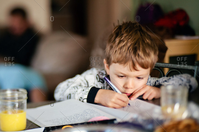 A little boy draws a picture in a book over breakfast