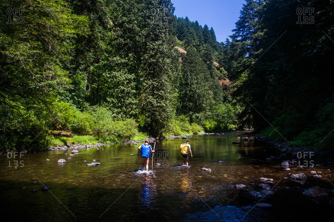 A couple hike in the middle of a creek carrying large dry bags in Columbia Gorge, Oregon