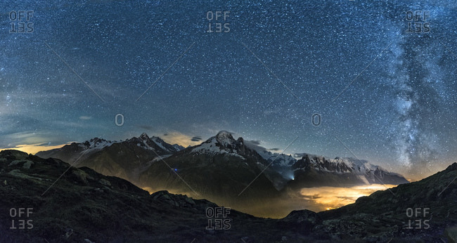 Milky way and Mount Blanc by night with the valley lighted by the lights of the town of Chamonix