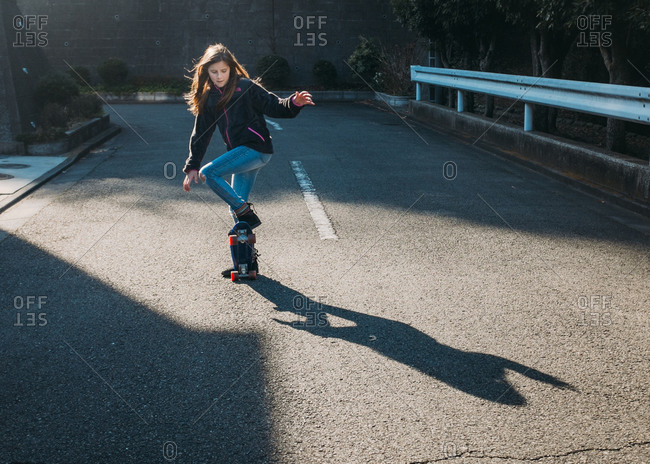 Girl doing trick on skateboard on side street