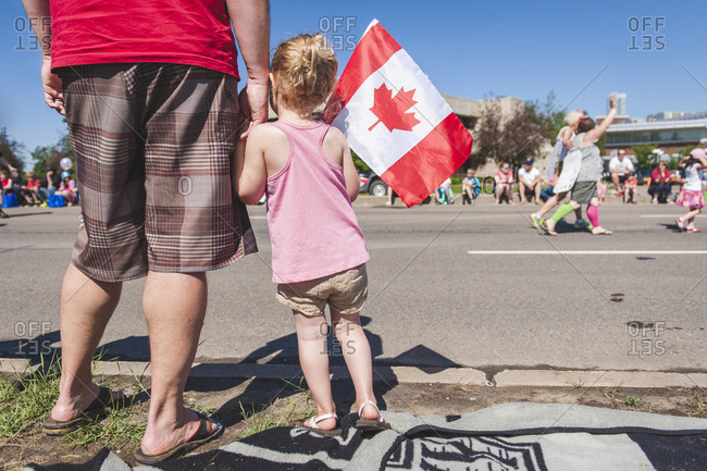 A little girl watches a parade while holding a Canadian flag