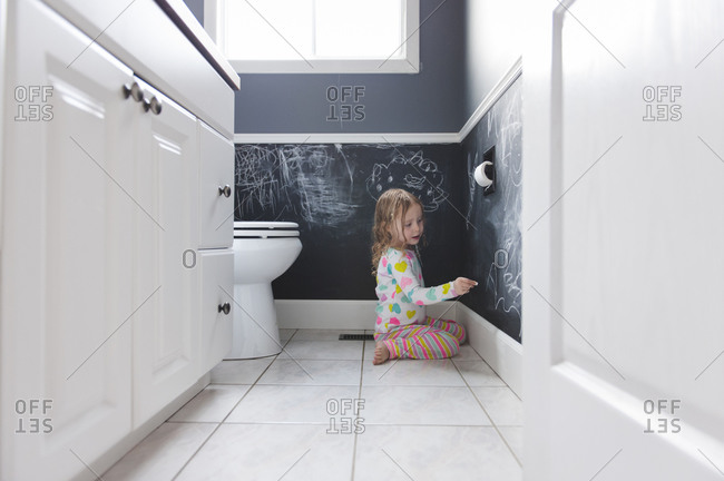 A little girl draws with chalk on her bathroom walls