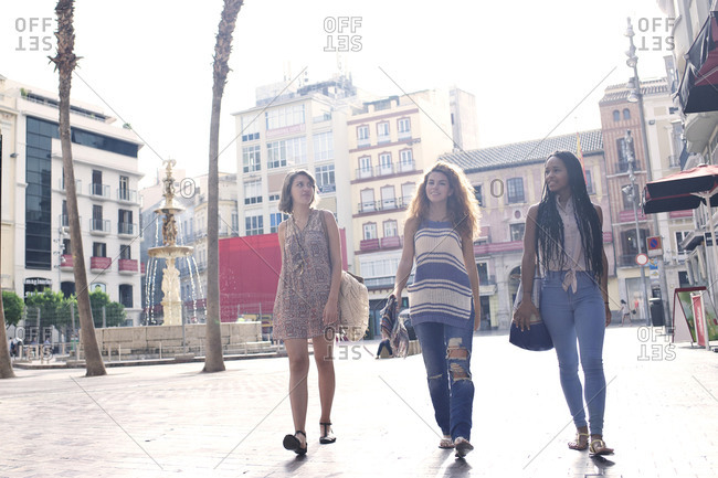 Three women walk past a fountain in a Spanish city square