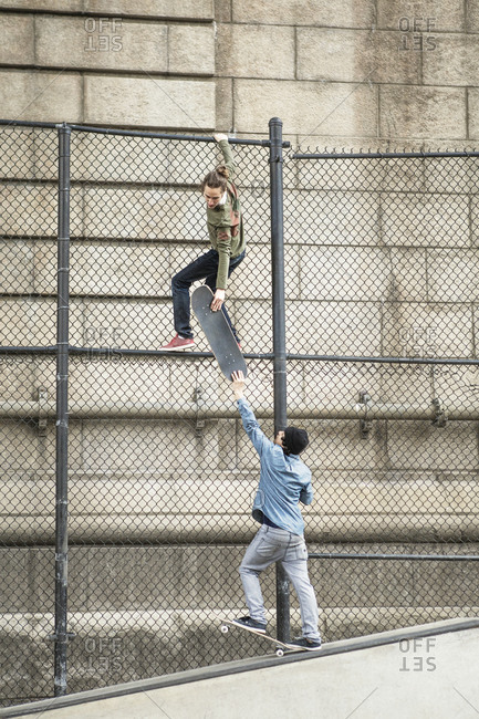Young men climbing over fence with skateboard