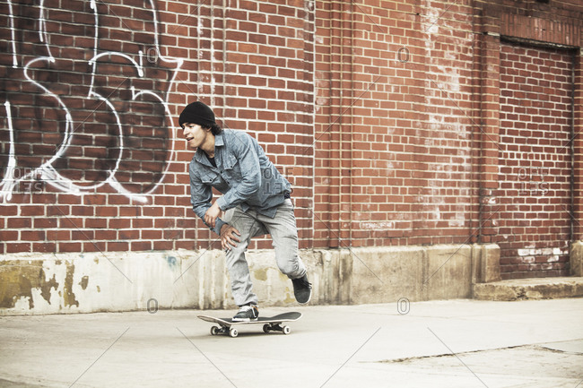 Young man riding skateboard down urban street