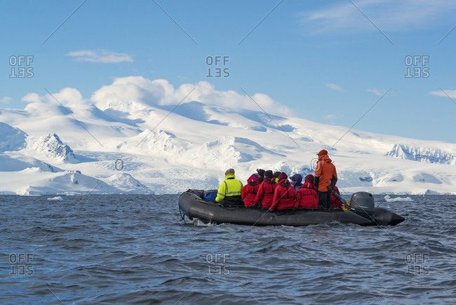 Group of people crossing the ocean in the Antarctic in a rubber boat with snow-covered mountains in the background
