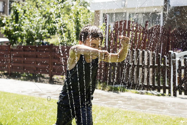 A boy running through a sprinkler a hot sunny day in summer