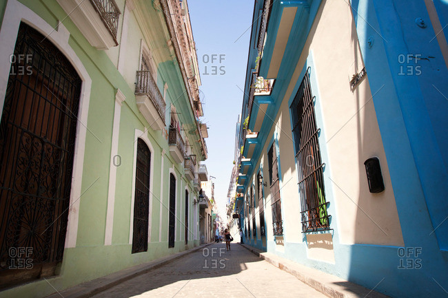 Woman walking down narrow alley with green and blue painted buildings on either side