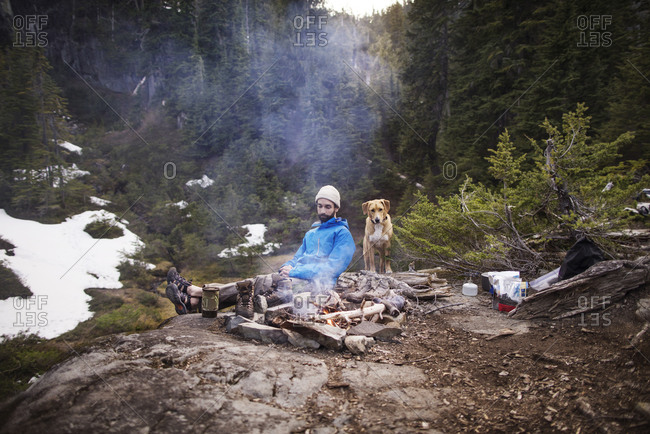 A man and his dog tend to a fire at a campsite