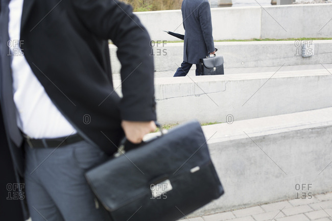 Two businessmen outdoors walking with briefcases