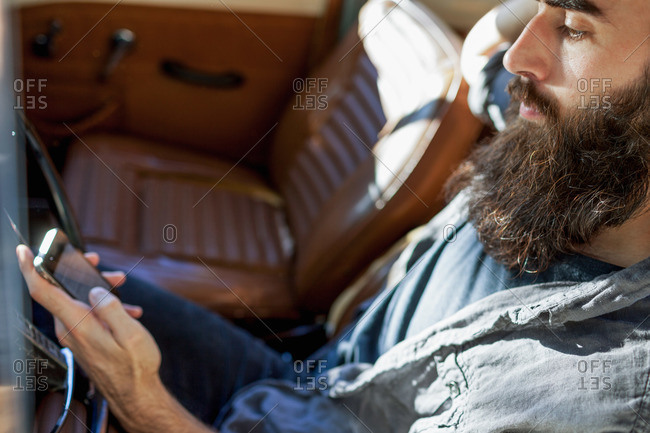 Bearded young man in vintage car using his smartphone
