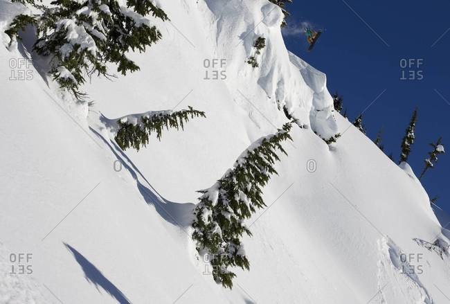 A snowboard flies off a cliff over clean white snow