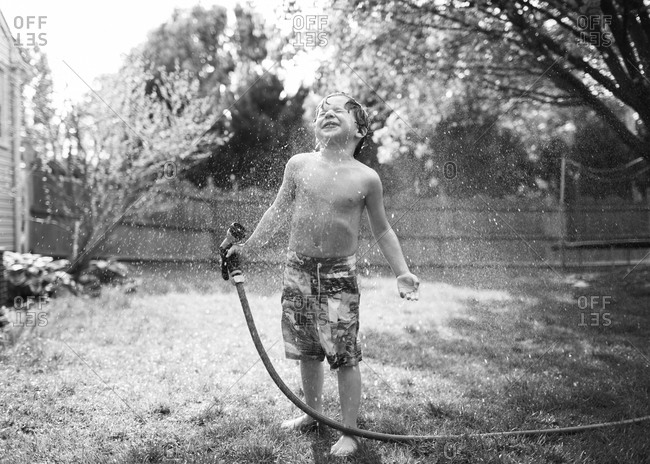 Young boys sprays himself with garden hose