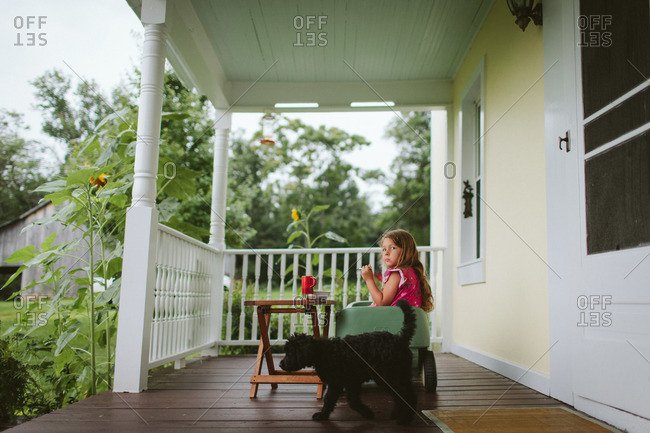 Little girl with snack on front porch by dog
