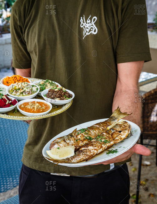 Server with fried fish and sides in Israeli restaurant